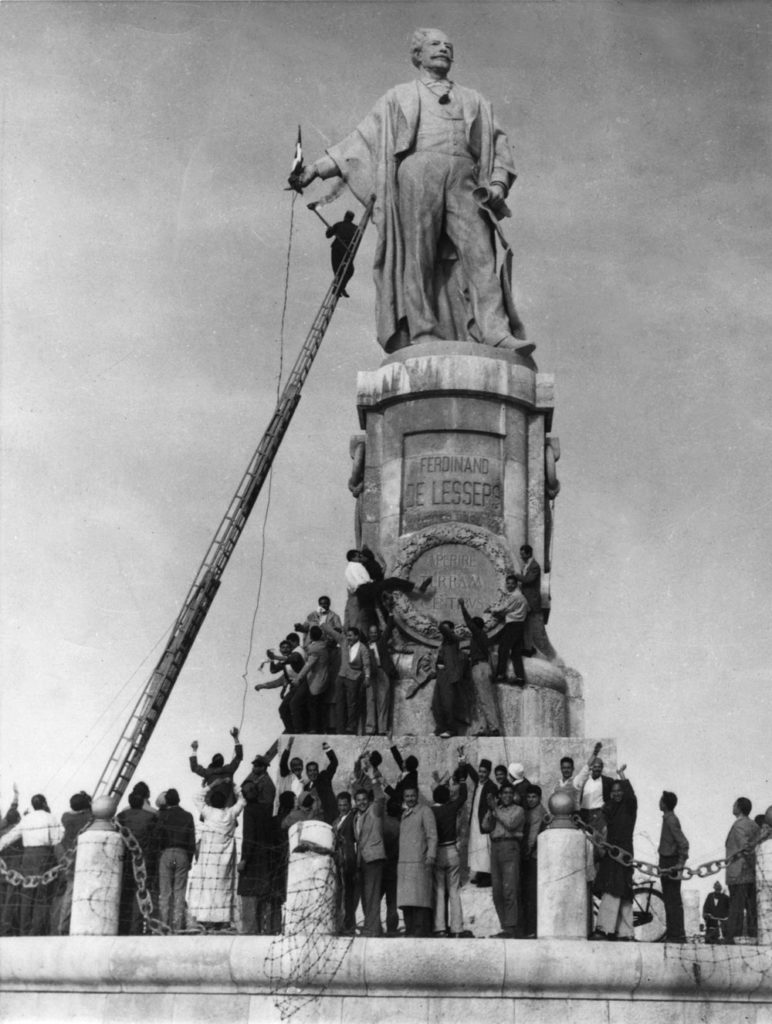 ภาพถ่ายในเดือนธันวาคม 1956 ชาวอียิปต์ปีนรูปปั้น Ferdinand de Lesseps (นักการทูตฝรั่งเศสผู้มีบทบาทสำคัญในการพัฒนาคลองสุเอซ) เพื่อนำธงชาติฝรั่งเศสมาเผาทำลาย (AFP PHOTO / AFP ARCHIVES)