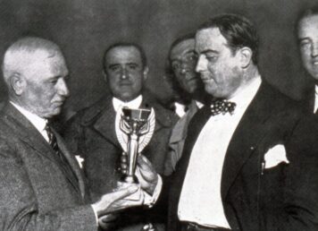 Jules Rimet (ซ้าย) มอบถ้วยรางวัลฟุตบอลโลกให้กับประธาน AUF, Raúl Jude ในปี 1930 ประกอบเรื่อง เทพีแห่งชัยชนะ